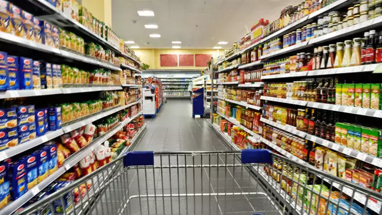 photo of a shopping cart in a grocery store aisle with fully stocked shelves