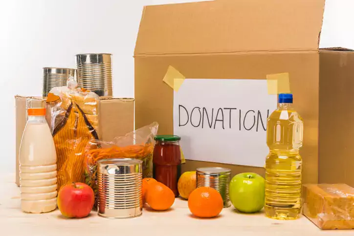 different food with cardboard box and donation sign on wooden table on white, donation concept