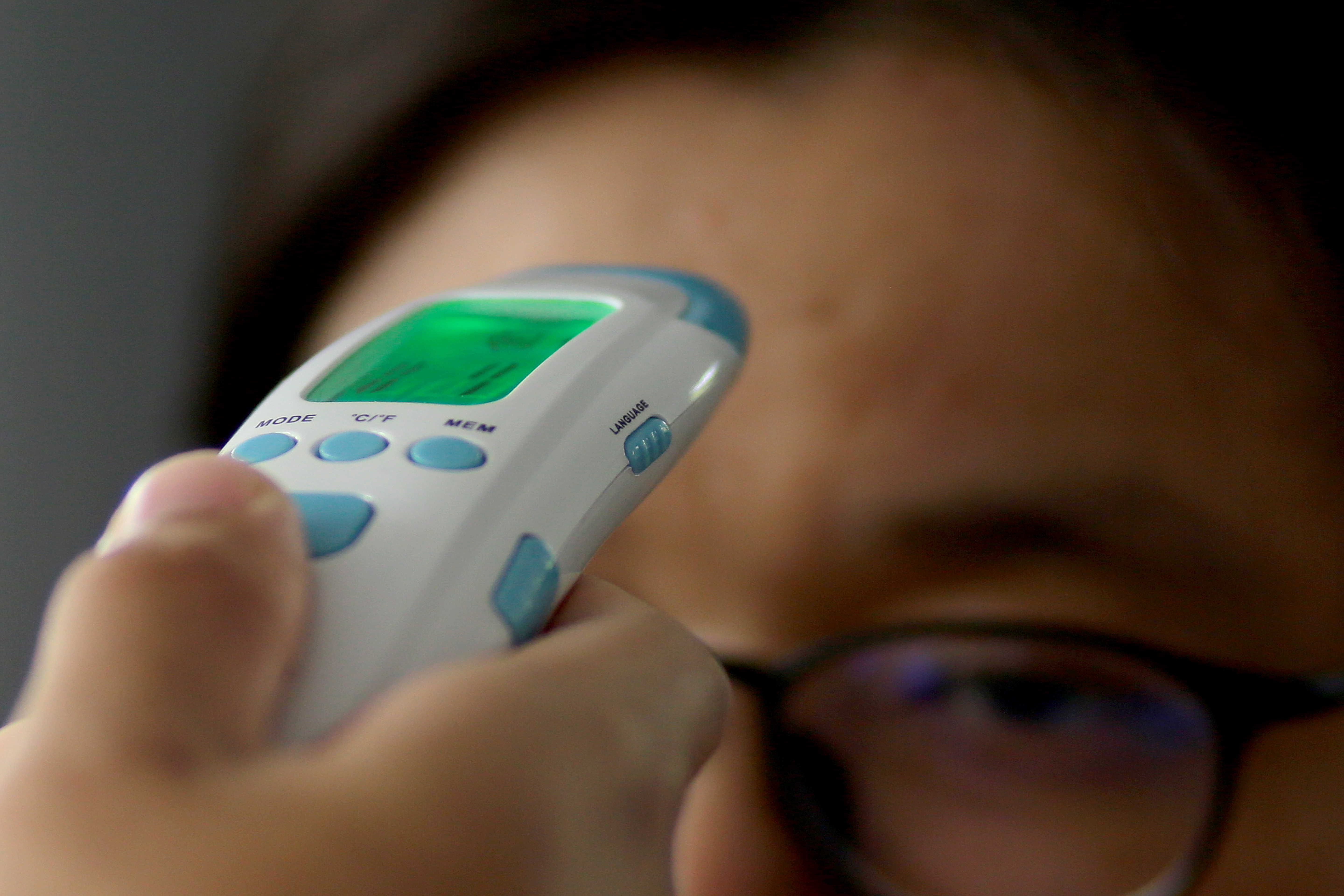 A woman wearing glasses getting her temperature taken.